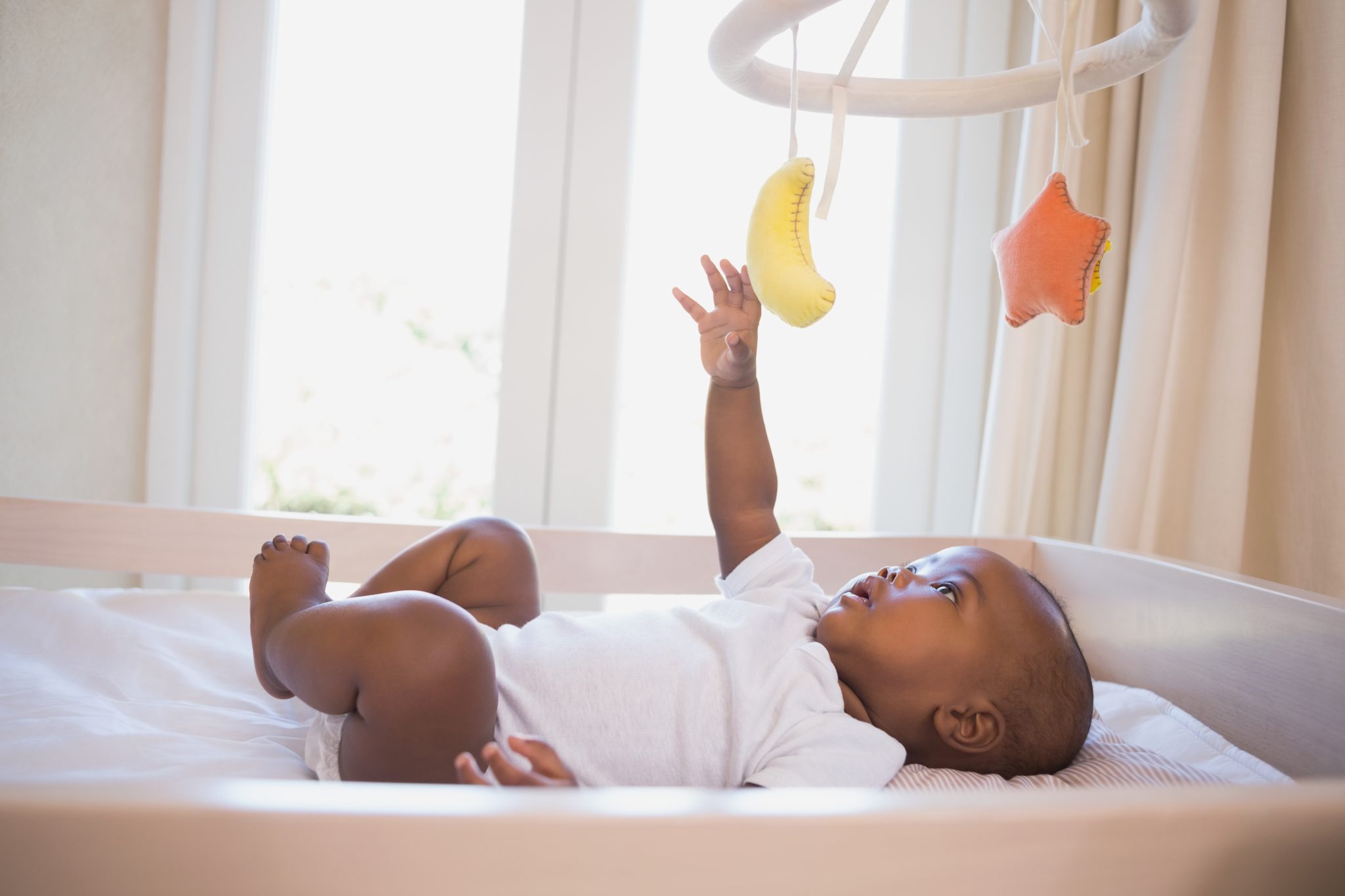 adorable-baby-boy-lying-in-his-crib-playing-with-mobile-consumer